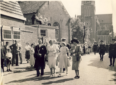 Wandeling door Asten, op weg naar het feestterrein. H.M. koningin Juliana en prinses Beatrix, in het gezelschap van Burgemeester Ploegmakers van Asten en echtgenote. Links het café van de Familie Knaapen met op de achtergrond de kerk van Asten