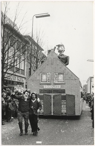 Carnaval 1965.Optocht. De groep voorstellend: de Brandweer op de Markt, gezien in de richting Veestraat, vooraan : twee leden v.d. vrijwillige brandweer. Links: Toon Nobels, rechts: Friedie Slegers