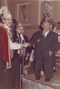 Martinus van Houts ontvangt een carnavalsonderscheiding van Prins Marini I, tijdens het bejaardenbal in zaal Wijlaars. In het midden vorst Pierre Corstjens